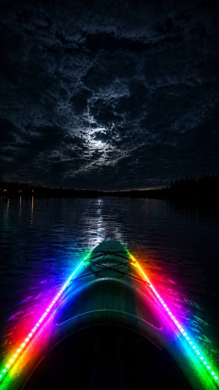 A kayak bow lined with RGB LED lights facing moonlit water.