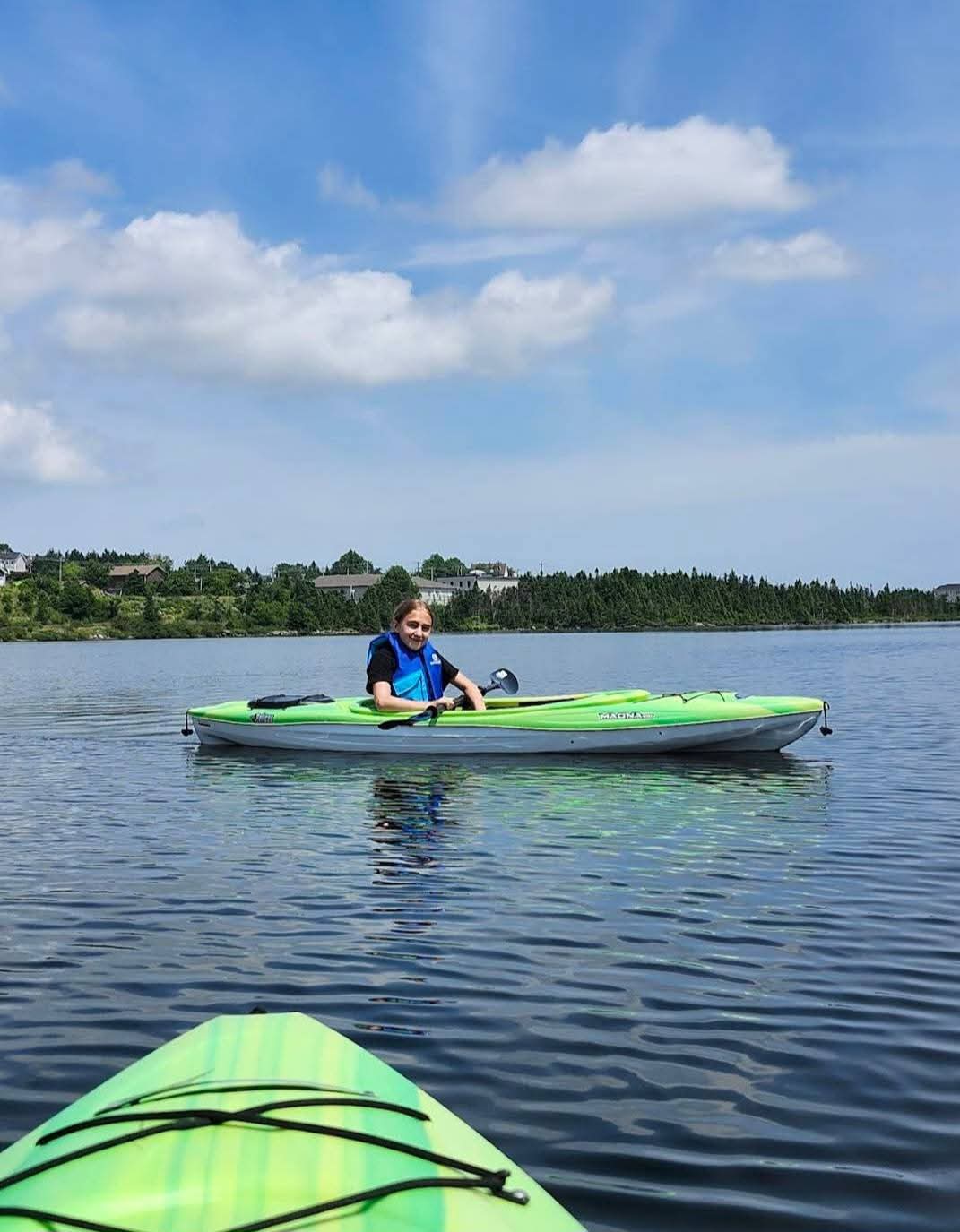 A young paddler in a green kayak on calm water at Neil's Pond.